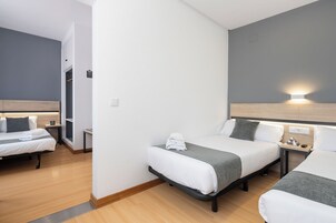 Quarto de hotel com duas camas, piso de madeira, paredes brancas e uma parede em cinza.