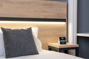 Ein Hotelzimmer mit einem hölzernen Kopfteil, einem Nachttisch mit einem Wi-Fi-Schild und einem grauen Kissen.
