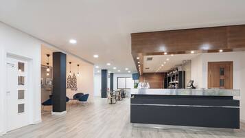A modern hotel lobby with a central reception desk, seating area, and a view of the city.