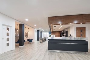Egy modern szállodai előcsarnok, központi recepcióval, pihenősarokkal és kilátással a városra.