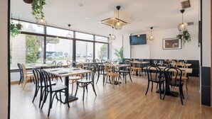 A spacious restaurant with wooden tables and chairs, large windows, hanging plants, and modern lighting fixtures. - Alda Puerto Seco (Burgos)
