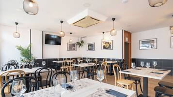 A restaurant interior with multiple tables, chairs, hanging lights, and wall-mounted artwork.