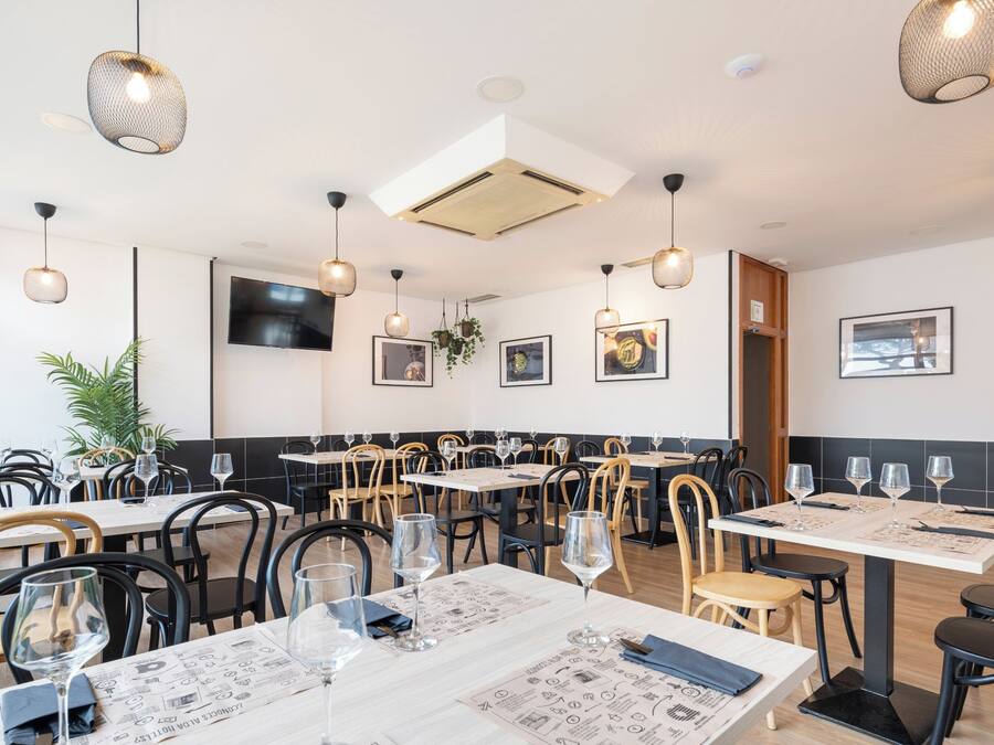 A restaurant interior with multiple tables, chairs, hanging lights, and wall-mounted artwork.