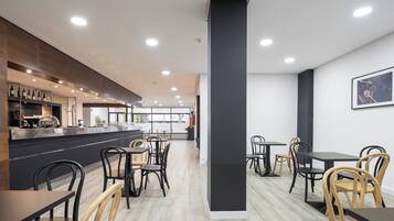 A modern cafe with a central pillar, wooden and black chairs, and a counter with wine bottles.