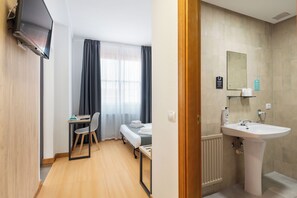 A hotel room with a bed, a desk with a chair, a television, and a bathroom with a sink and mirror. - Alda Puerto Seco (Burgos)