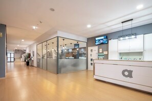 A modern reception area with a glass partition, a reception desk, and a mounted television. - Alda Puerto Seco (Burgos)