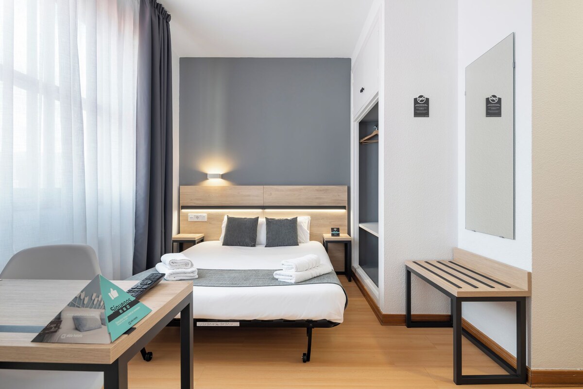 A hotel room with a bed, bedside tables, a desk, and a mirror.