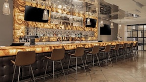 Eine Bar mit einer langen Theke, mehreren Barhocker und einer Auswahl an Flaschen und Gläsern.