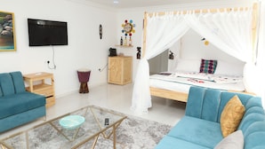 A bedroom with a bed under a canopy, a TV mounted on the wall, a wooden nightstand, a blue sofa, and a glass coffee table.