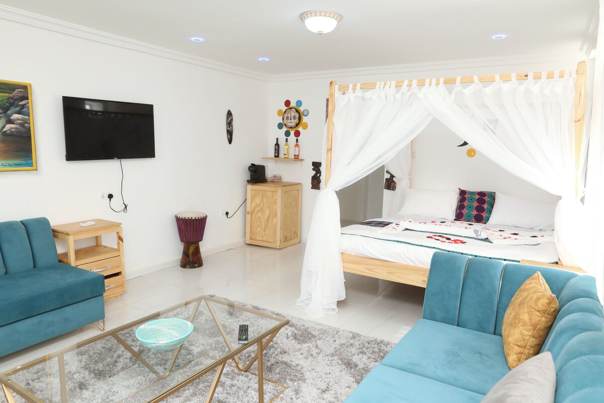 Une chambre à coucher avec un lit sous un dais, un téléviseur fixé au mur, une table de chevet en bois, un canapé bleu et une table basse en verre.