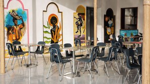 A dining area with a long table and multiple chairs, surrounded by colorful murals on the walls.