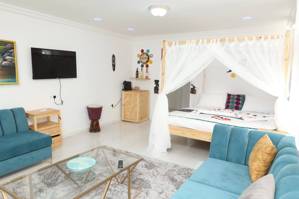 Une chambre à coucher avec un lit sous un dais, un téléviseur fixé au mur, une table de chevet en bois, un canapé bleu et une table basse en verre.