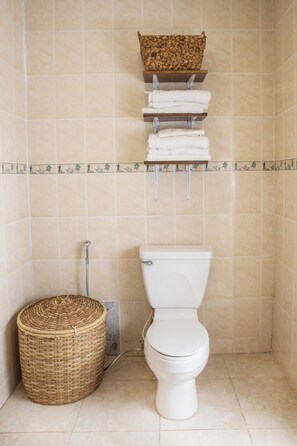 Un baño con inodoro, una cesta de mimbre y un estante con toallas.