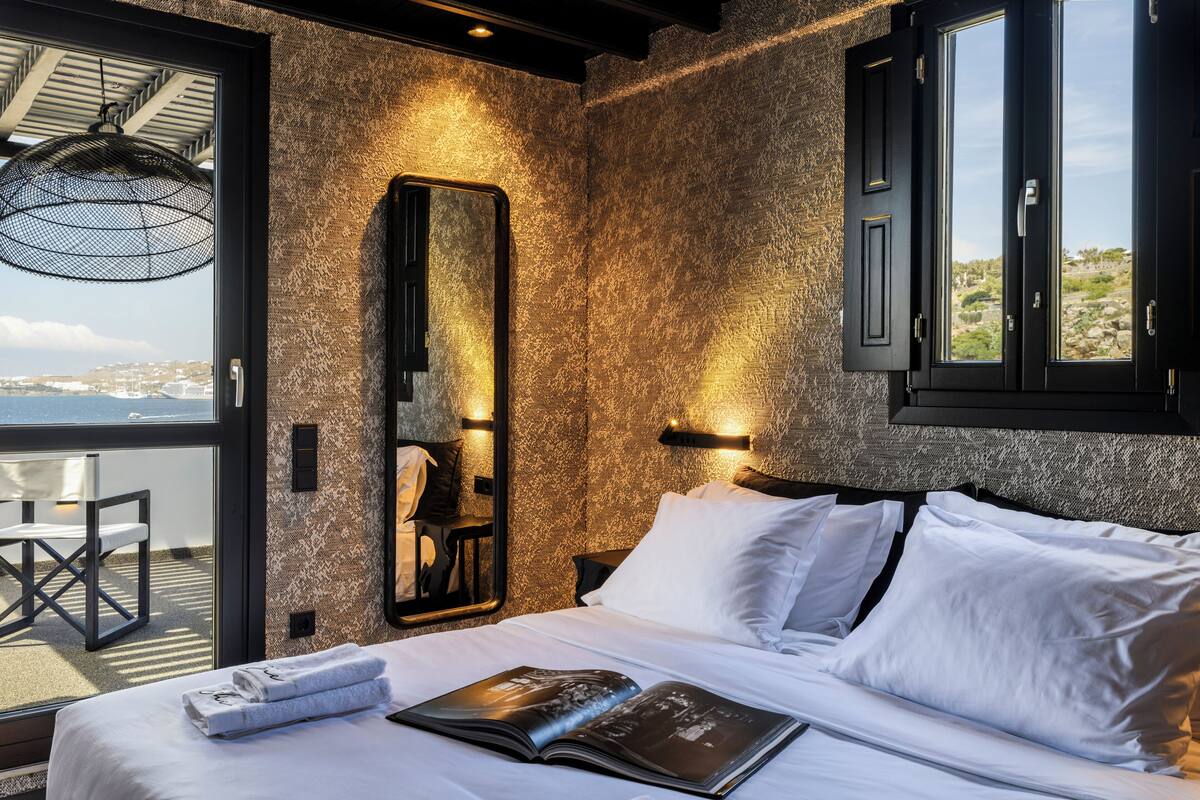 Ein Schlafzimmer mit einem großen Bett, Meerblick, einer Essecke mit Tisch und Stühlen sowie einer Wand mit Struktur.