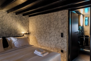 A hotel room with a textured wall, a neatly made bed with white linens, and a visible bathroom with a sink and mirror.