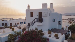 Un bâtiment blanc avec un escalier menant à un balcon, entouré de cactus et de bougainvilliers.