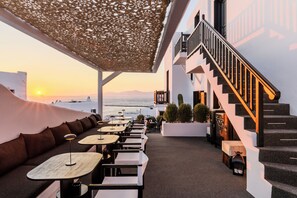 Un espace extérieur aménagé avec des tables et des chaises, un escalier et une vue sur la mer au coucher du soleil.