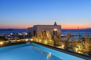 Une vue sur la piscine avec un coucher de soleil sur la mer, un bâtiment doté d’une tour et un paysage urbain en arrière-plan.