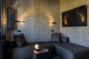 A modern room with a textured wall, a flat-screen TV mounted on the wall, a sofa with cushions, and a small table with a lamp and a book.