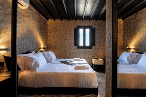 Een kamer met twee bedden, een muur met stenen textuur, een raam met zonwering en wandlampen.