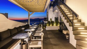 Une terrasse sur le toit avec des sièges extérieurs, un escalier et une vue sur le coucher de soleil sur la mer.