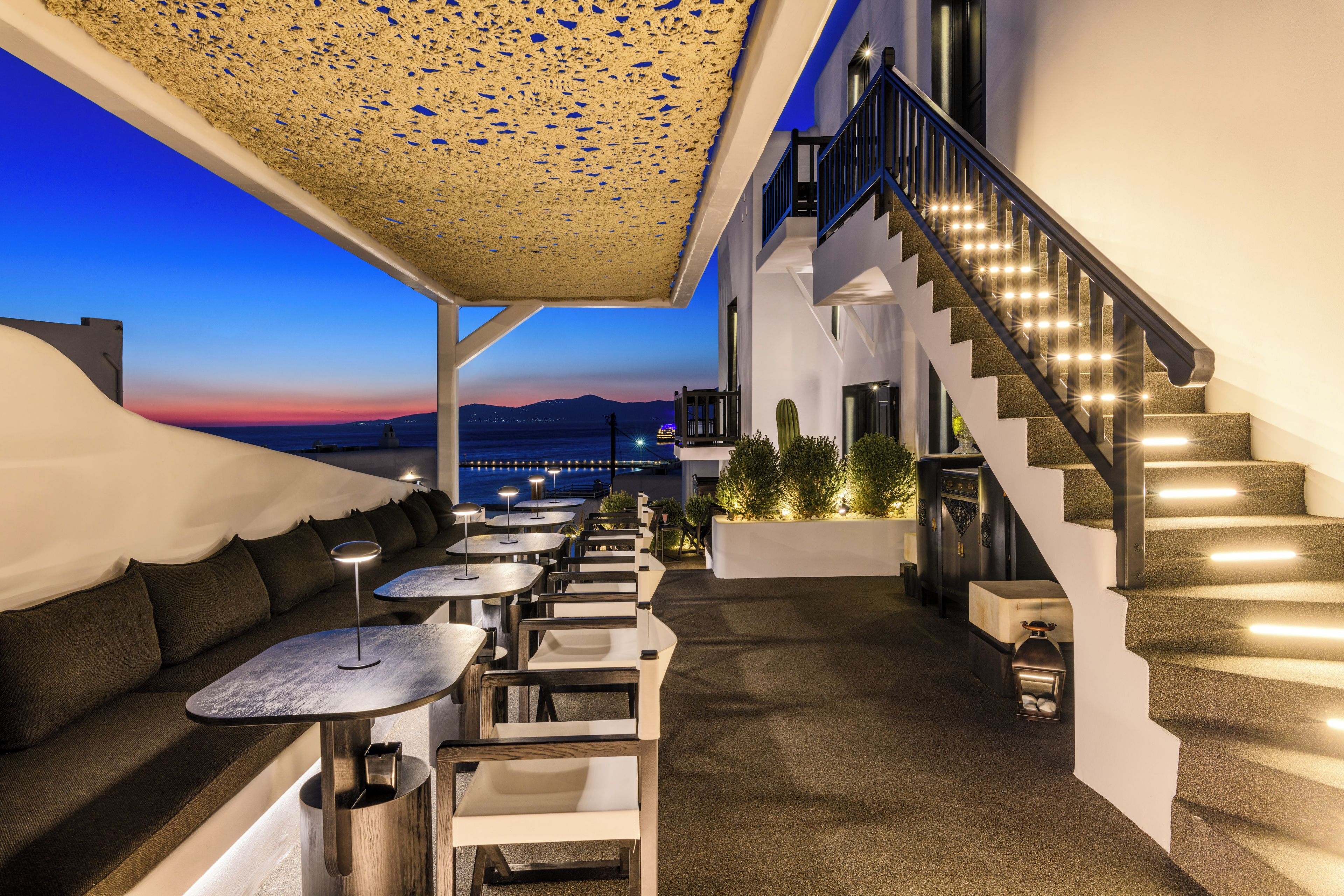 Une terrasse sur le toit avec des sièges extérieurs, un escalier et une vue sur le coucher de soleil sur la mer.