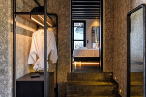 Une salle de bain moderne avec un grand miroir, un peignoir suspendu à un porte-manteau et un lit recouvert d’une courtepointe blanche.