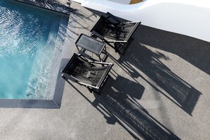 Un espace aménagé au bord de la piscine, comprenant une piscine rectangulaire, deux chaises longues et un parasol.
