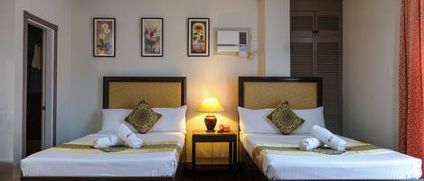 A hotel room with two beds, a nightstand with a lamp, and three framed artworks on the wall.