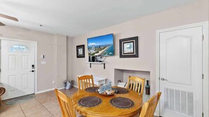 A dining room with a round wooden table, four chairs, a ceiling fan, a white door, and a framed picture on the wall.
