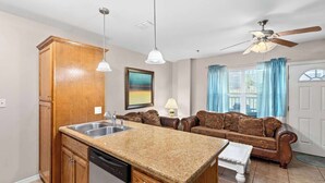 A compact kitchen with granite countertops, a dishwasher, and a dining area with a brown leather sofa.