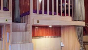 A multi-level wooden cabin with a staircase connecting the floors, each with a red bed and purple pillows.