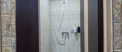Zona de ducha con paredes de azulejos y suelo estampado, ducha de mano y grifo empotrado.