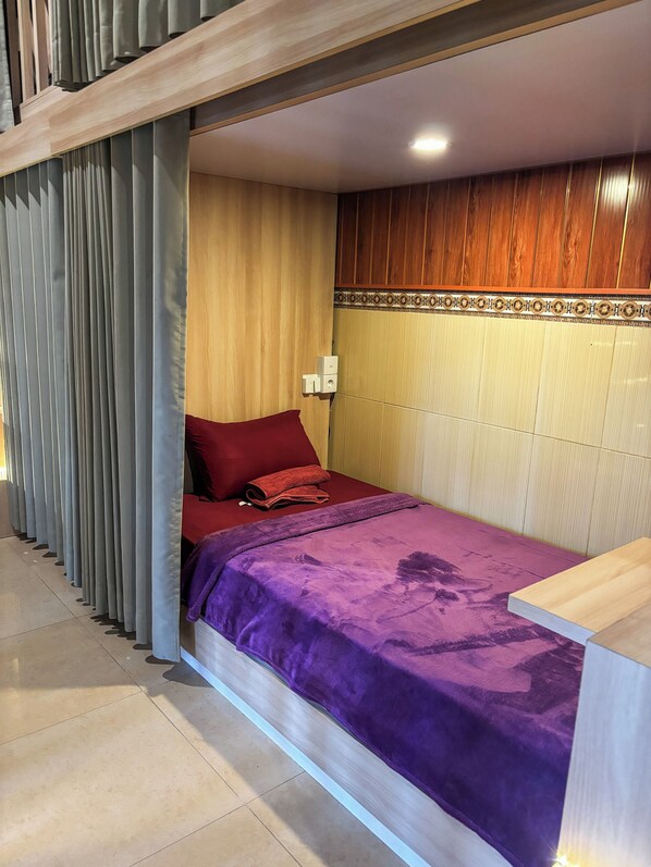 A bedroom with a bed, a wooden headboard, a red pillow, a purple blanket, and a wooden floor.