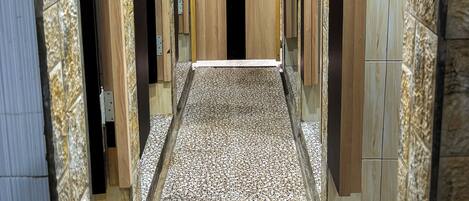 A hallway with a central wooden door, flanked by wooden panels and stone-like flooring.