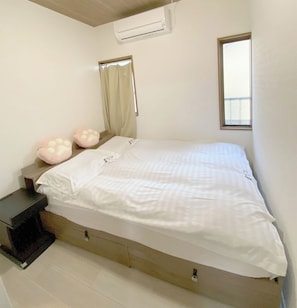 A bedroom with a bed, a nightstand, a window, and an air conditioning unit.