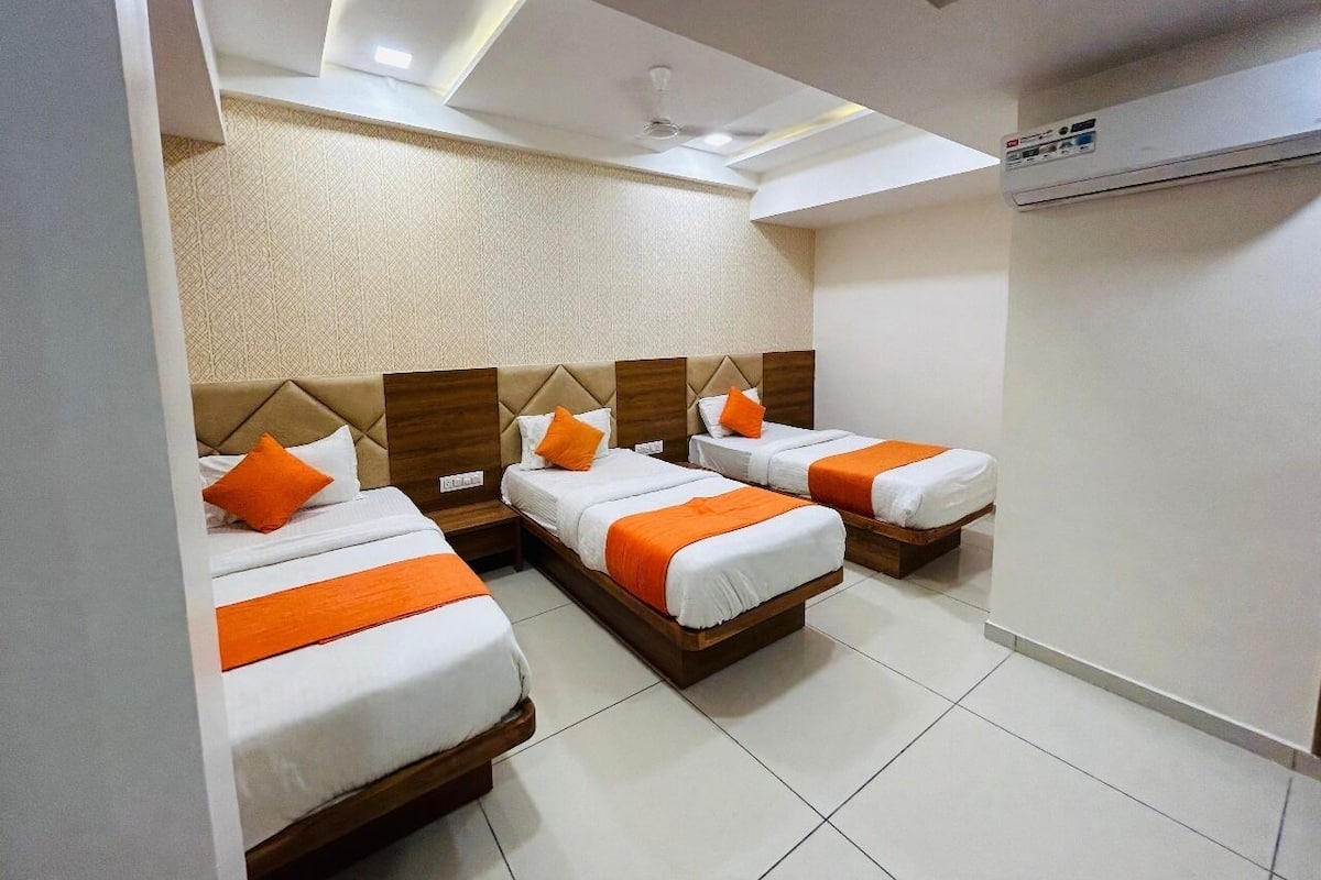 A hotel room with three beds, each with white bedding and orange accents, a ceiling fan, and an air conditioning unit.