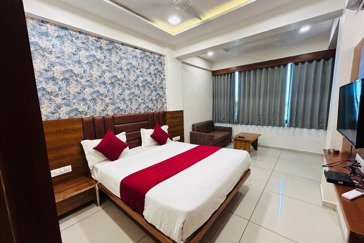 A hotel room with a large bed, a wooden headboard, a TV, and a small seating area.