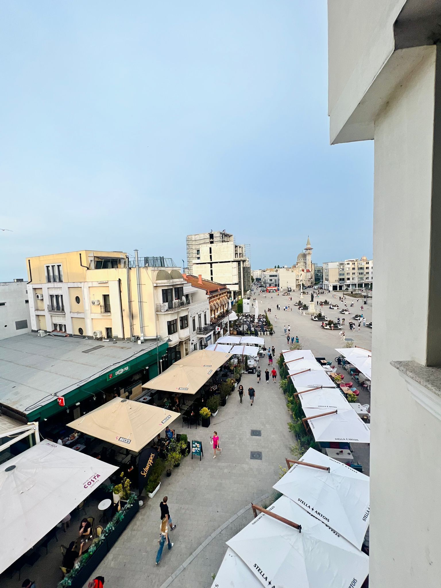 Un mercado al aire libre animado con varias toldas blancas, gente caminando y diversos edificios al fondo.