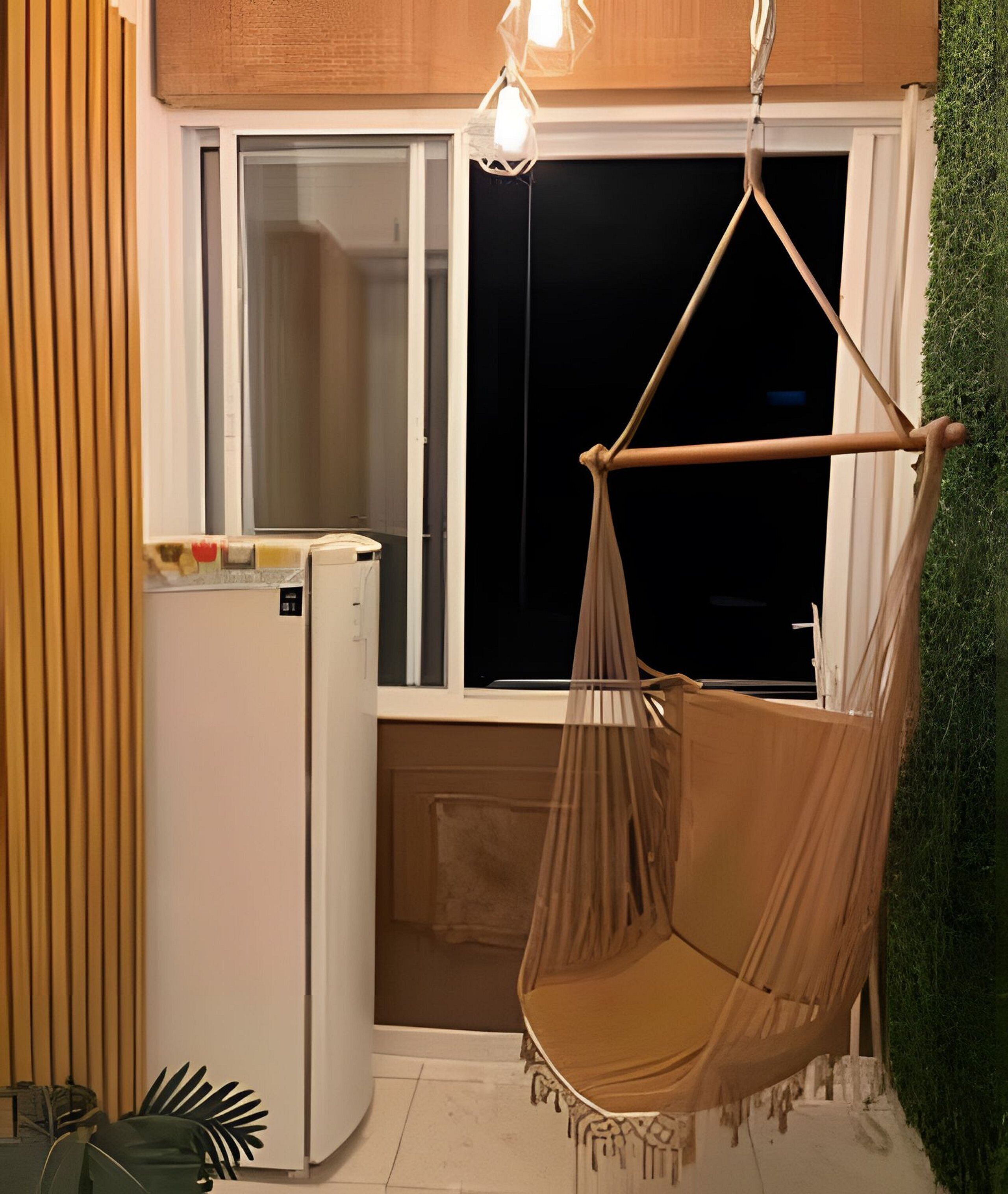 A room with a hanging chair, a white refrigerator, and a window with a view of the outside.