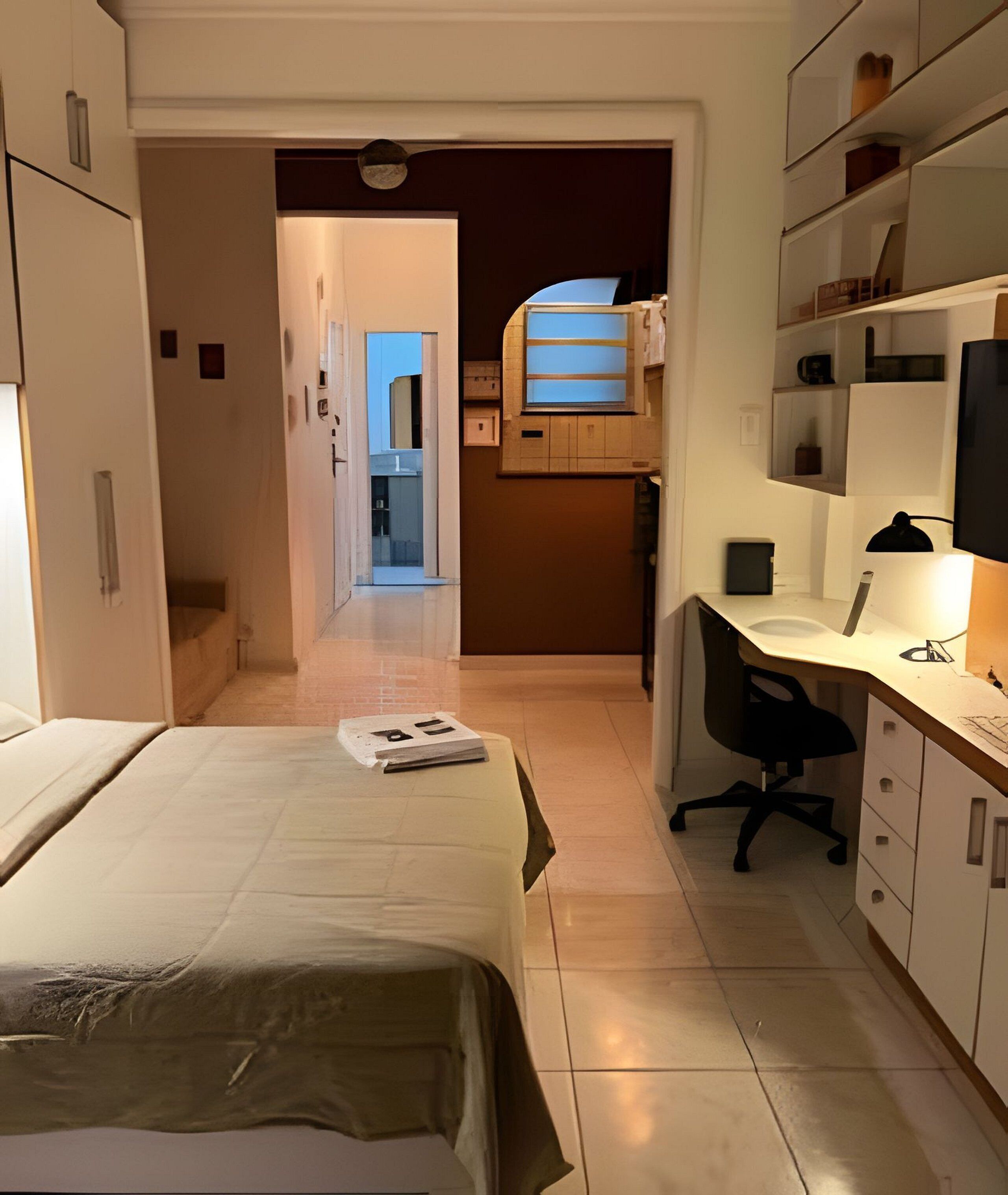 A hotel room with a bed, a desk, and a chair. There is a bathroom visible in the background.