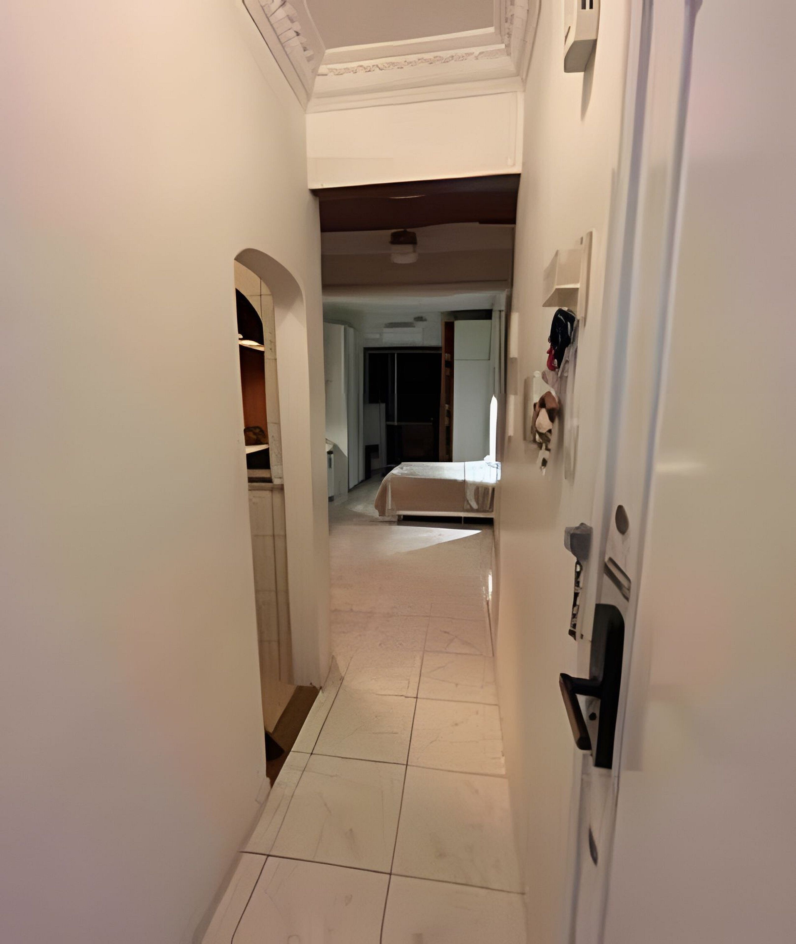 Un pasillo estrecho con suelo de baldosas que conduce a un dormitorio con cama y armario.
