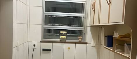 A compact kitchen with a gas stove, a window with blinds, and a small shelf above the stove.