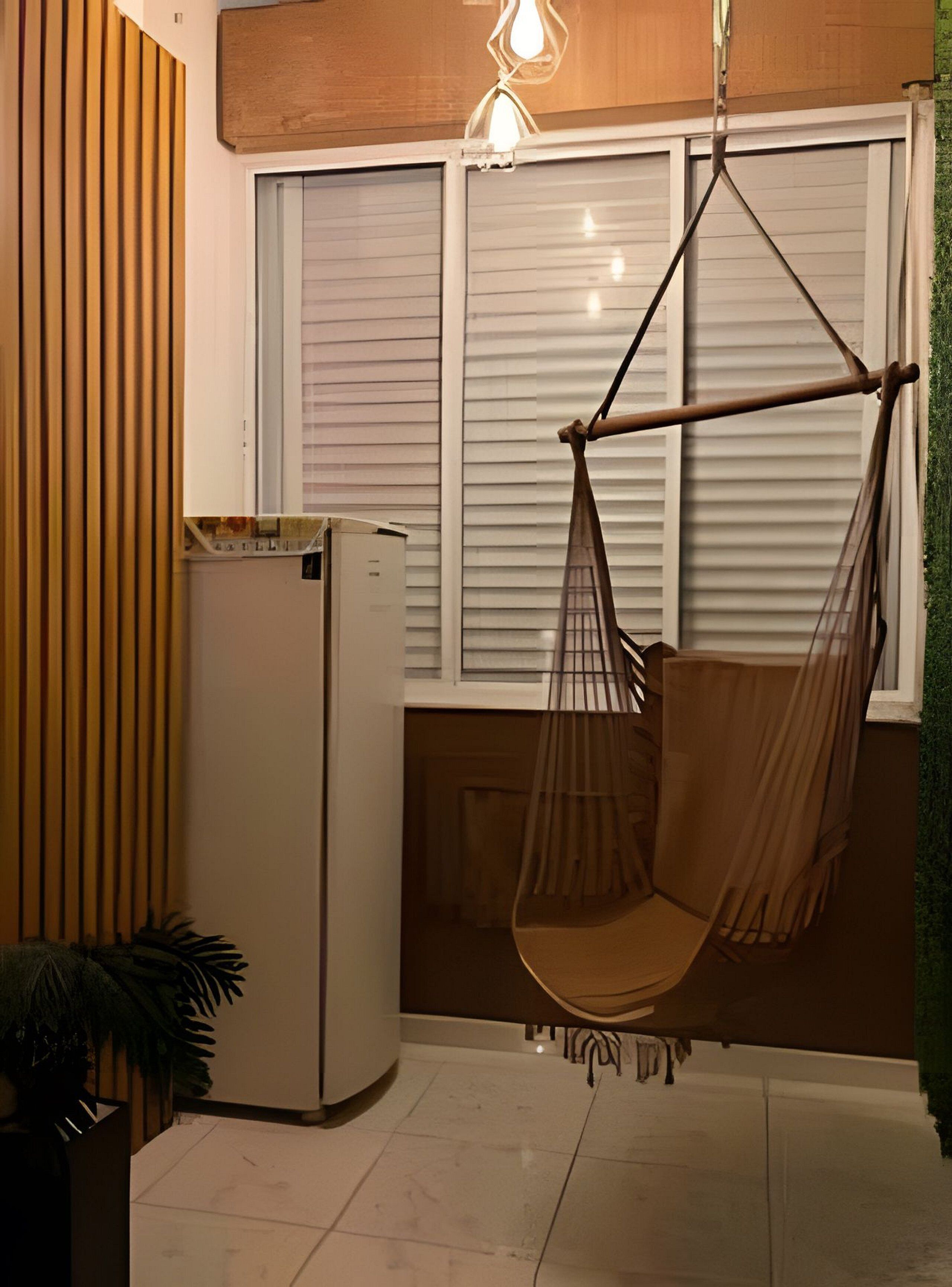 A room with a hanging chair, a refrigerator, and a window with blinds.