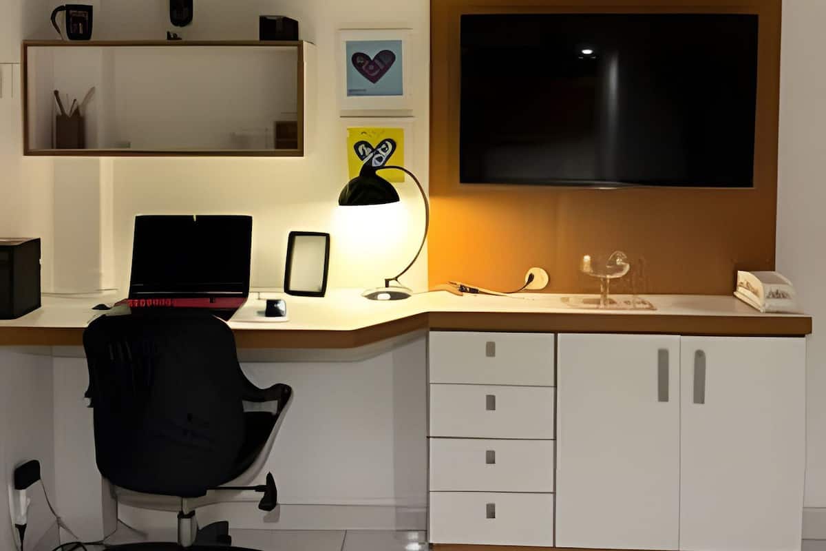 Ett modernt kontorsutrymme med ett skrivbord, en dator, en stol, hyllor med dekorativa föremål och en stor TV.