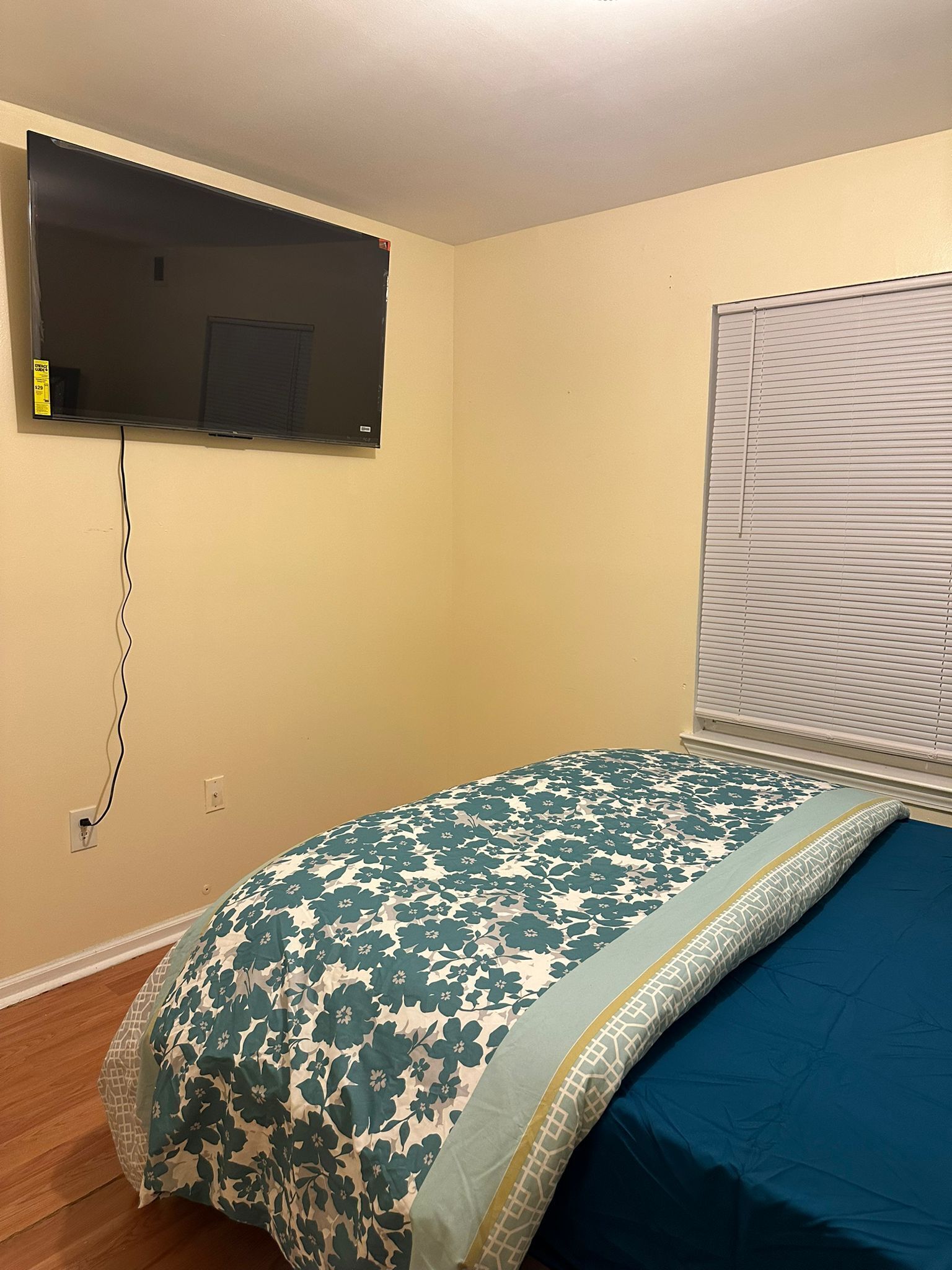 Ein Schlafzimmer mit einem Bett, einem Wand-Fernseher und einem Fenster mit Jalousien.