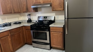 A kitchen with wooden cabinets, a stainless steel stove, a refrigerator, and a blender on the counter. - NWK 457  ROOM 112-B (Newark)
