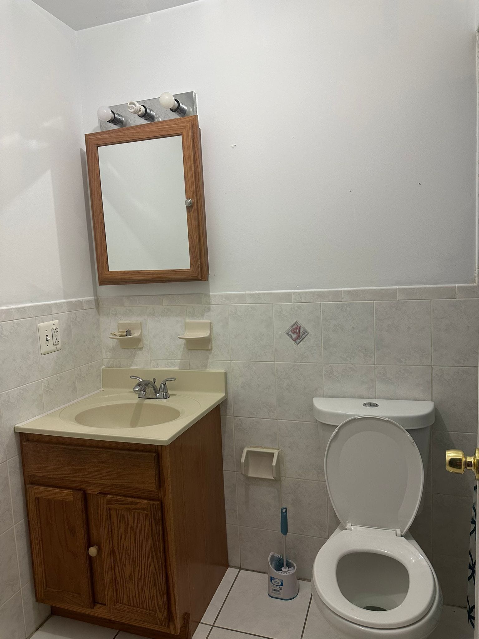 A bathroom with a wooden cabinet, a sink, a mirror, and a toilet.