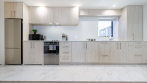 A modern kitchen with light wood cabinets, a stainless steel refrigerator, an oven, and a window providing natural light.