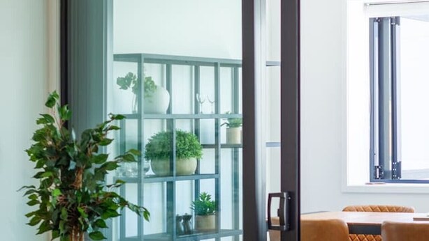 A modern living room with a glass door leading to a balcony, a leather sofa, a round coffee table, and a woven ottoman.